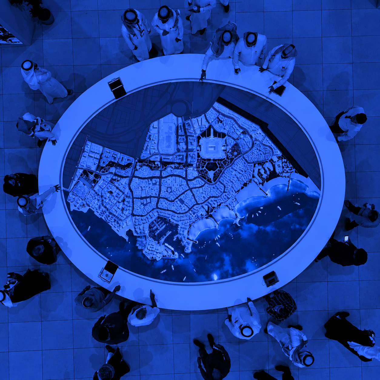 Visitors around a circular architectural masterplan model, seen from above in blue and black duotone.